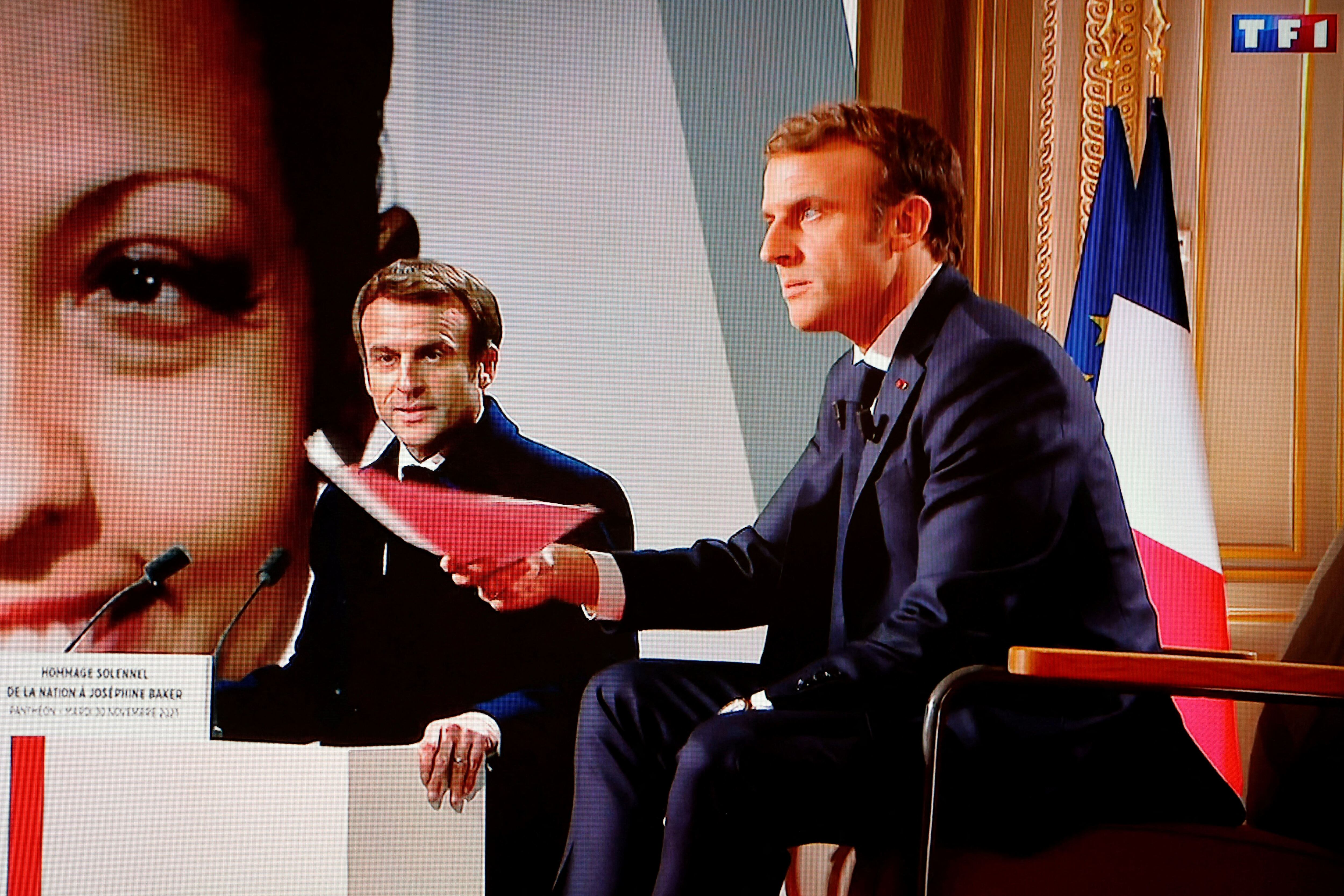 El presidente Emmanuel Macron hace un gesto frente a una pantalla que lo muestra, durante una entrevista en el Palacio del Elíseo en París.