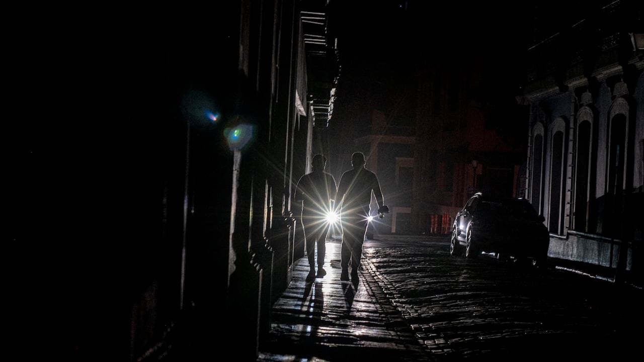 En esta foto de archivo tomada el 6 de abril de 2022, se ven los faros de un automóvil junto a personas que caminan en la oscuridad en San Juan, Puerto Rico, después de que un gran corte de energía azotara la isla.