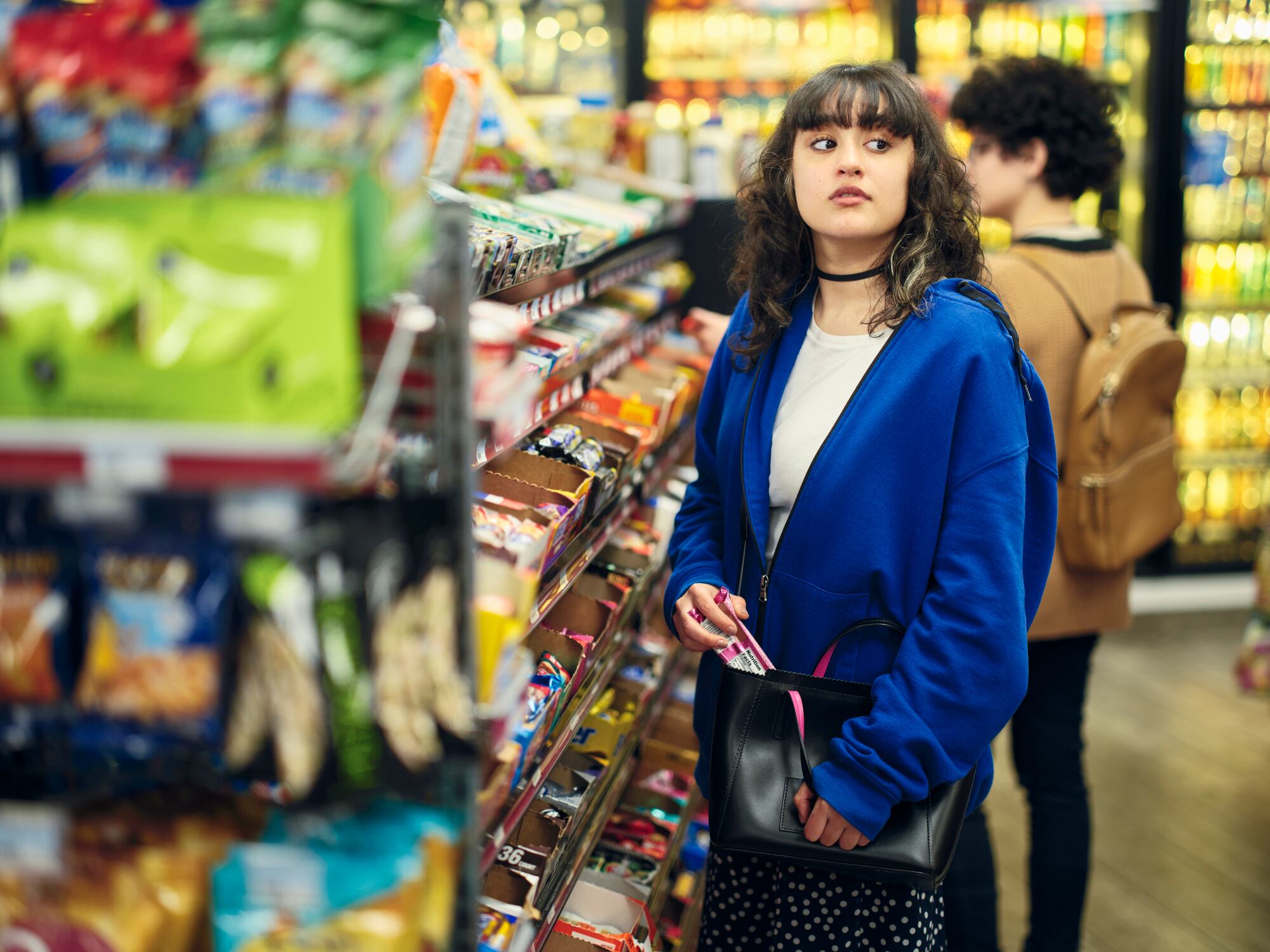 A young woman shoplifting (stealing) merchandise in a convenience store.