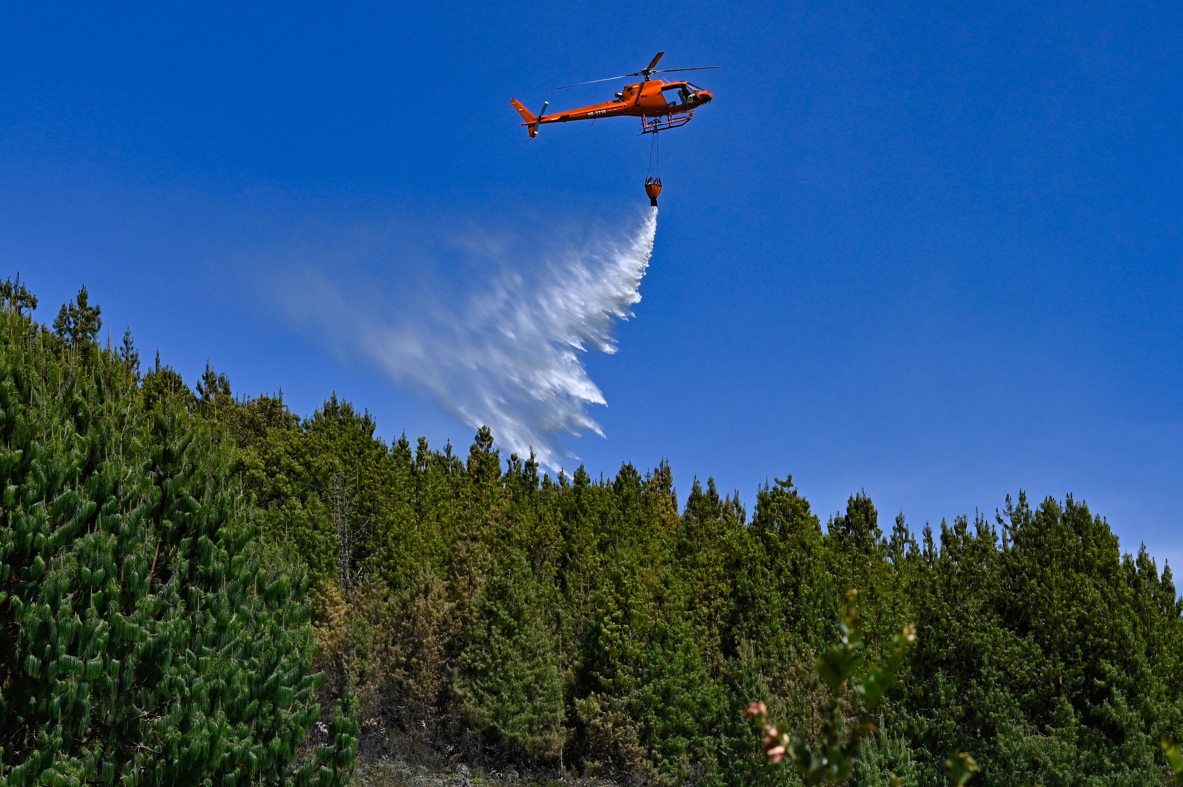 A helicopter drops water to put out a forest fire in Nemocon, Colombia on January 26, 2024. Yesterday Colombia asked the member countries of the United Nations for help to extinguish around thirty forest fires that are ravaging several regions and drowning the capital, Bogota, in smoke. (Photo by Luis ACOSTA / AFP)
