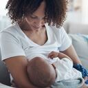 Una foto de una joven amamantando a su adorable bebé en el sofá de casa