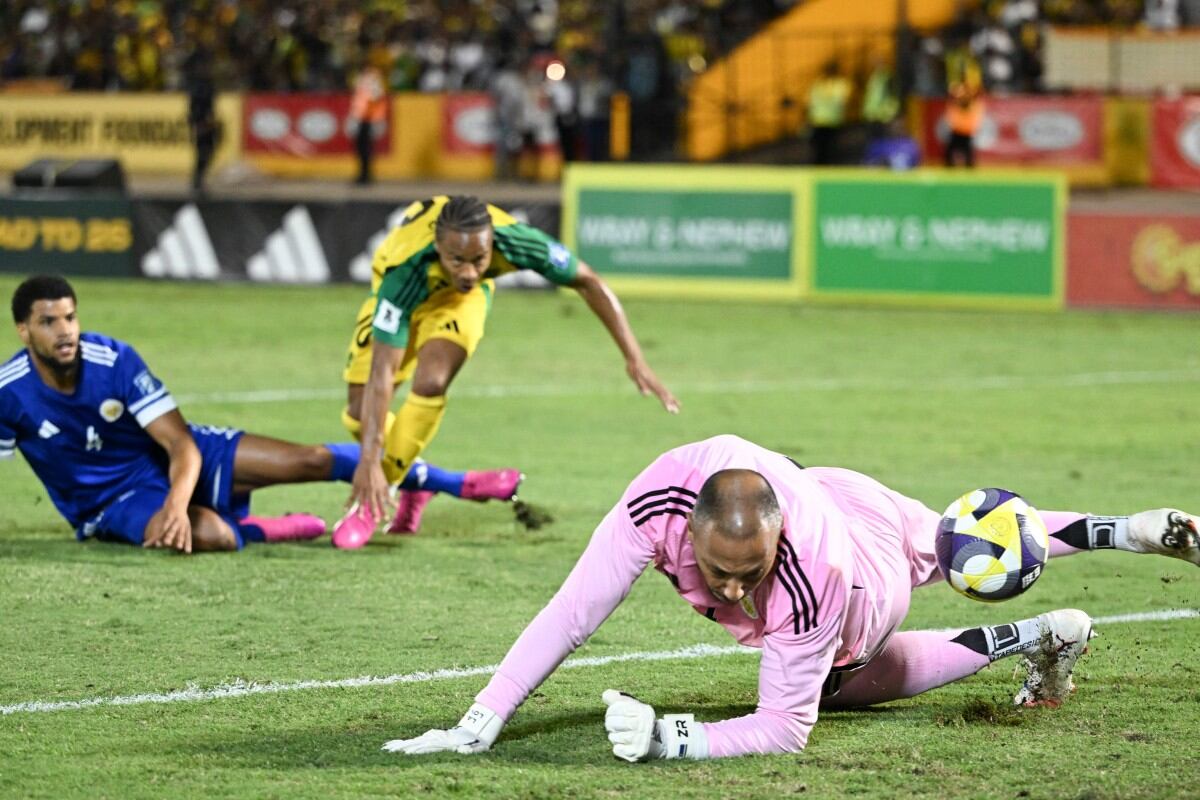 El portero #01 de Curazao, Eloy Room (R), salva un intento de gol del delantero #10 de Jamaica, Bobby Reid (C), durante el partido de fútbol clasificatorio para la Copa Mundial entre Jamaica y Curazao en el Estadio Nacional de Kingston, Jamaica, el 18 de noviembre de 2025
