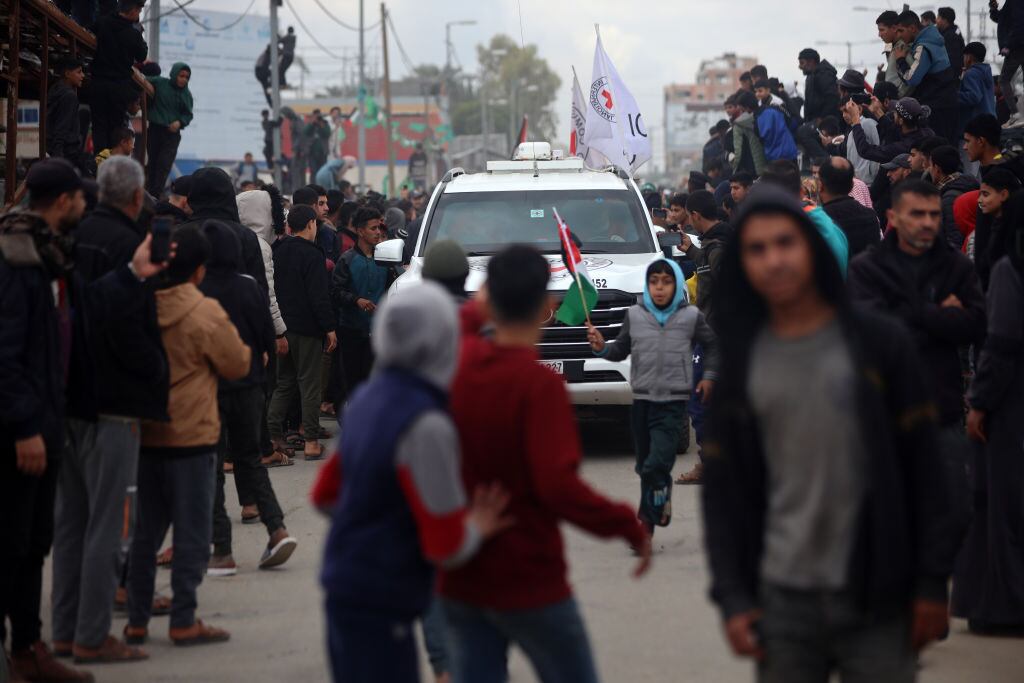 Palestinians gather beside a street and some climb up on a billboard stand to watch Hamas fighters hand over three Israeli hostages to a Red Cross team in Deir el-Balah, central Gaza, on February 8, 2025. Hamas militants hand over three Israeli hostages on February 8, as part of the fifth exchange under a fragile Gaza ceasefire, with 183 prisoners held by Israel due to be released later in the day. (Photo by Majdi Fathi/NurPhoto via Getty Images)