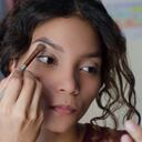 Mujer hermosa joven aplicando sombra de ojos con una brocha de maquillaje en el hueso de la frente