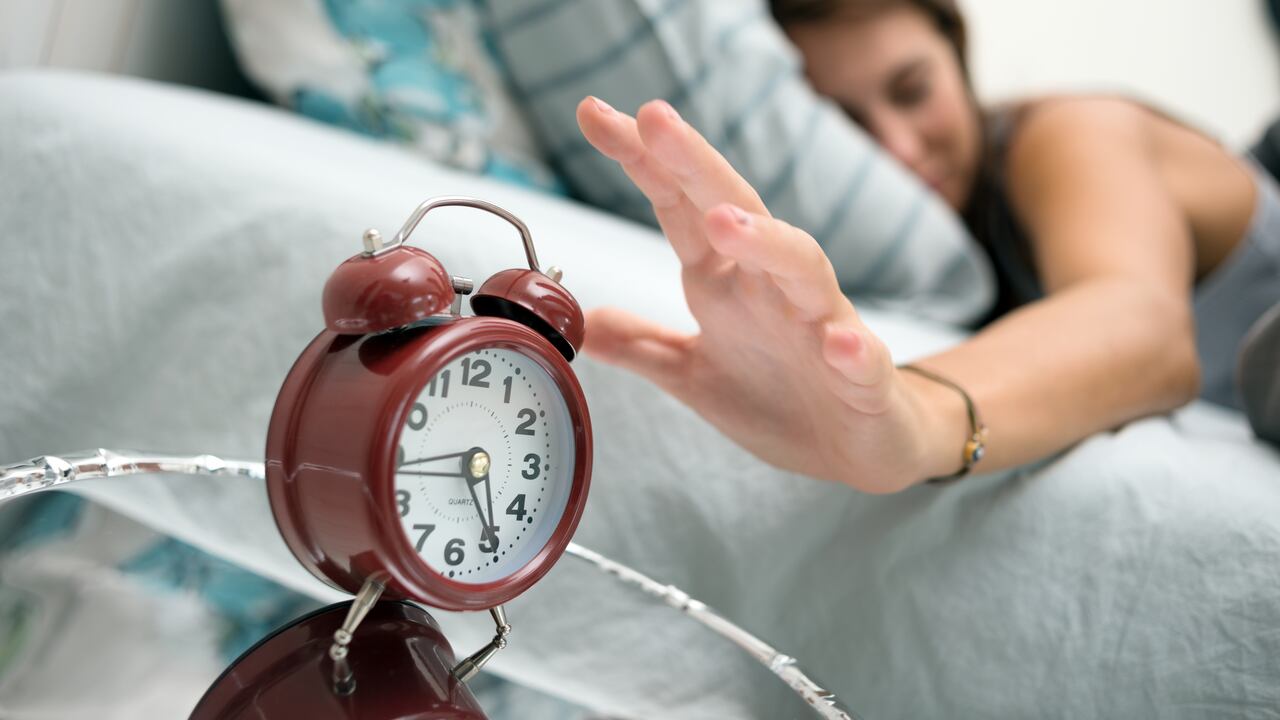 Mujer despertando con reloj despertador. Foto: Getty Images.