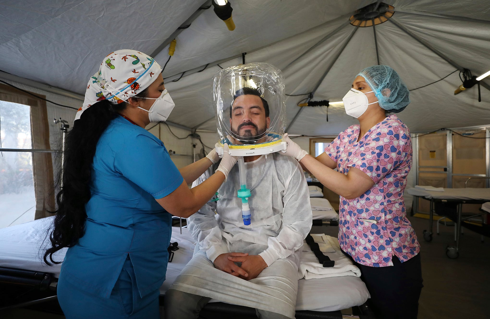 La terapeuta respiratoria Dalis Johana Ramirez, izquierda, y la terapeuta Belkis Melgarejo, ajustan un casco Ecleris NIV / CPAP a un compañero de trabajo del hospital mientras demuestran a la prensa cómo funciona debajo de una lona donde el Hospital El Tunal abrió más camas este mes en medio del COVID- 19 pandemia en Bogotá, Colombia, jueves 21 de enero de 2021. El hospital dice que compraron 12 de los cascos que dan tratamiento con oxígeno. (Foto AP / Fernando Vergara)