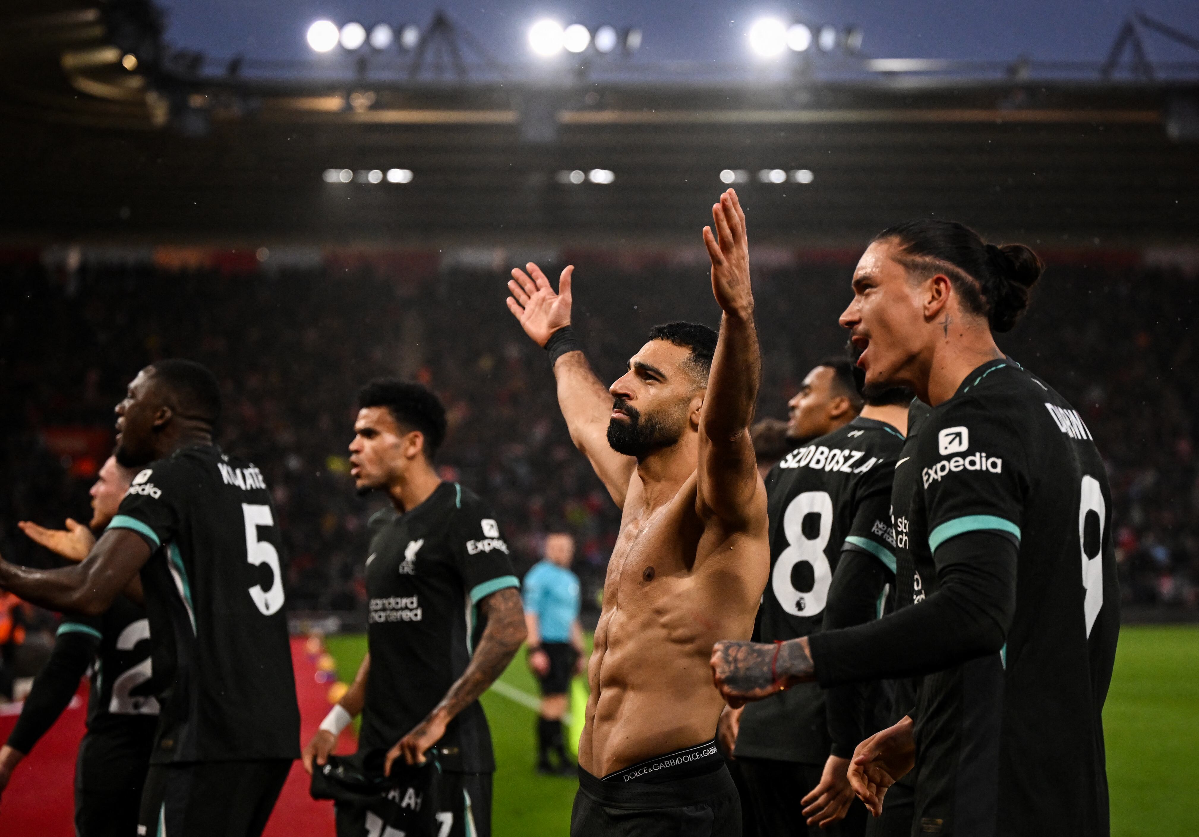 Liverpool's Egyptian striker #11 Mohamed Salah (C) celebrates with teammates and supporters after shooting a penalty kick and scoring his team third goal during the English Premier League football match between Southampton and Liverpool at St Mary's Stadium in Southampton, southern England on November 24, 2024. (Photo by JUSTIN TALLIS / AFP) / RESTRICTED TO EDITORIAL USE. No use with unauthorized audio, video, data, fixture lists, club/league logos or 'live' services. Online in-match use limited to 120 images. An additional 40 images may be used in extra time. No video emulation. Social media in-match use limited to 120 images. An additional 40 images may be used in extra time. No use in betting publications, games or single club/league/player publications. /