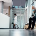 Hombre mayor angustiado con mascarilla mientras está sentado solo en el pasillo del hospital. Copie el espacio.