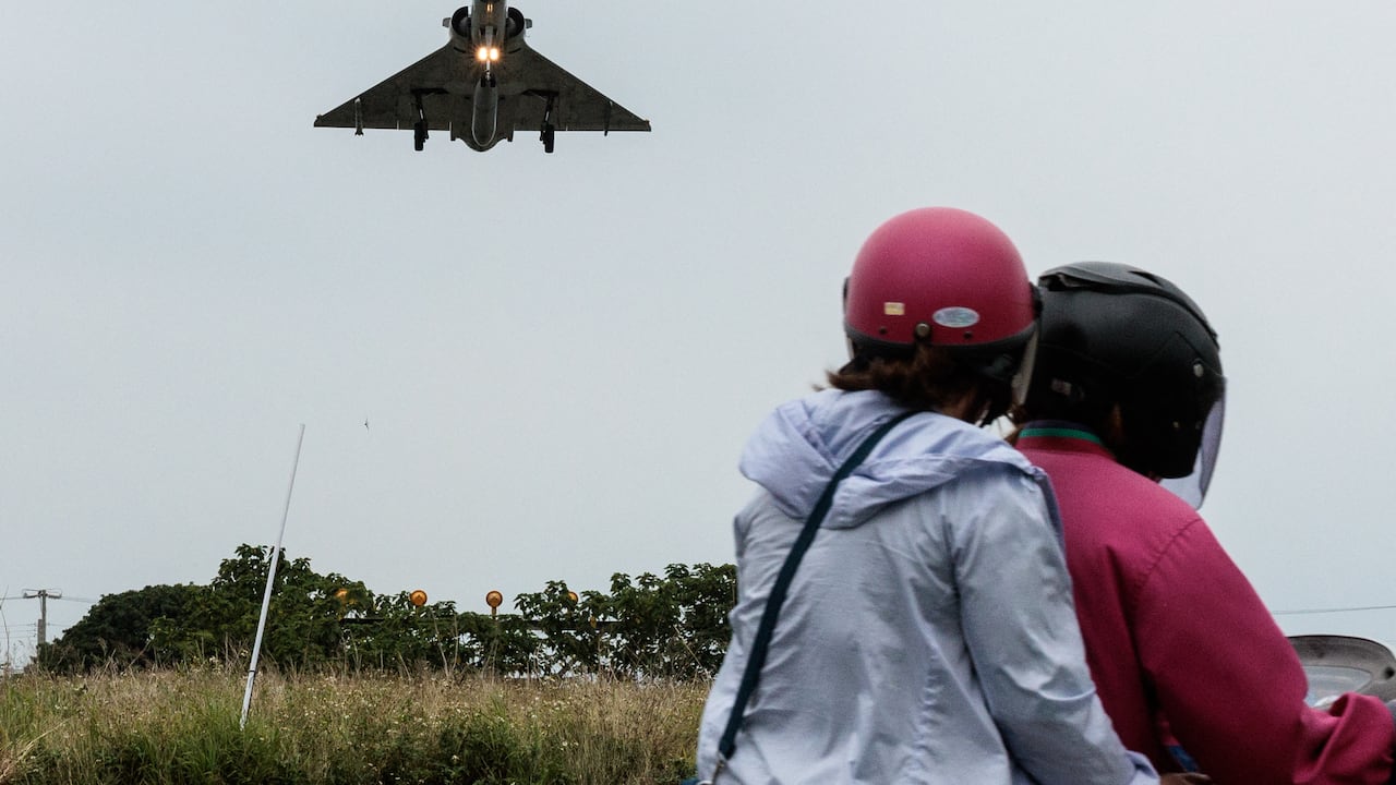 Dos personas viajan en motocicleta mientras un avión de combate Mirage 2000 de la Fuerza Aérea de Taiwán se acerca para aterrizar en una base de la fuerza aérea en Hsinchu, en el norte de Taiwán, el 23 de mayo de 2024.