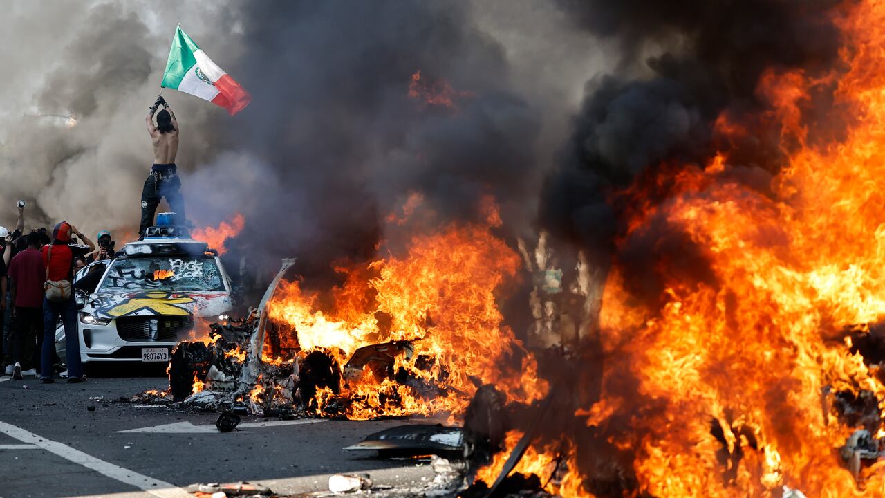 Manifestante ondea la bandera mexicana sobre un carro vandalizado en medio de las protestas contra la ICE.