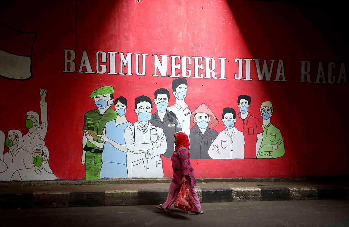 Una mujer pasa junto a un mural con temática del coronavirus en honor a los médicos y demás trabajadores esenciales, en Yakarta, Indonesia, el miércoles 26 de agosto. Los escritos en el mural dicen "Nuestro cuerpo y alma para el país". Foto: Dita Alangkara / AP  
