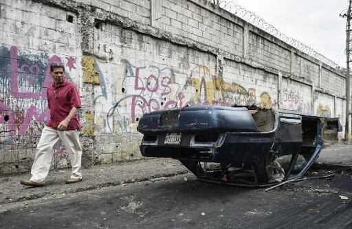 Un hombre pasa al lado de un carro incinerado, minutos antes de que inicie la gran marcha de la oposición. Créditos: LUIS ROBAYO / AFP.