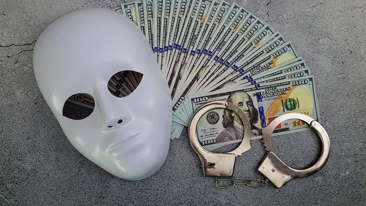 Handcuffs made of hundred-dollar bills with a White plastic mask.