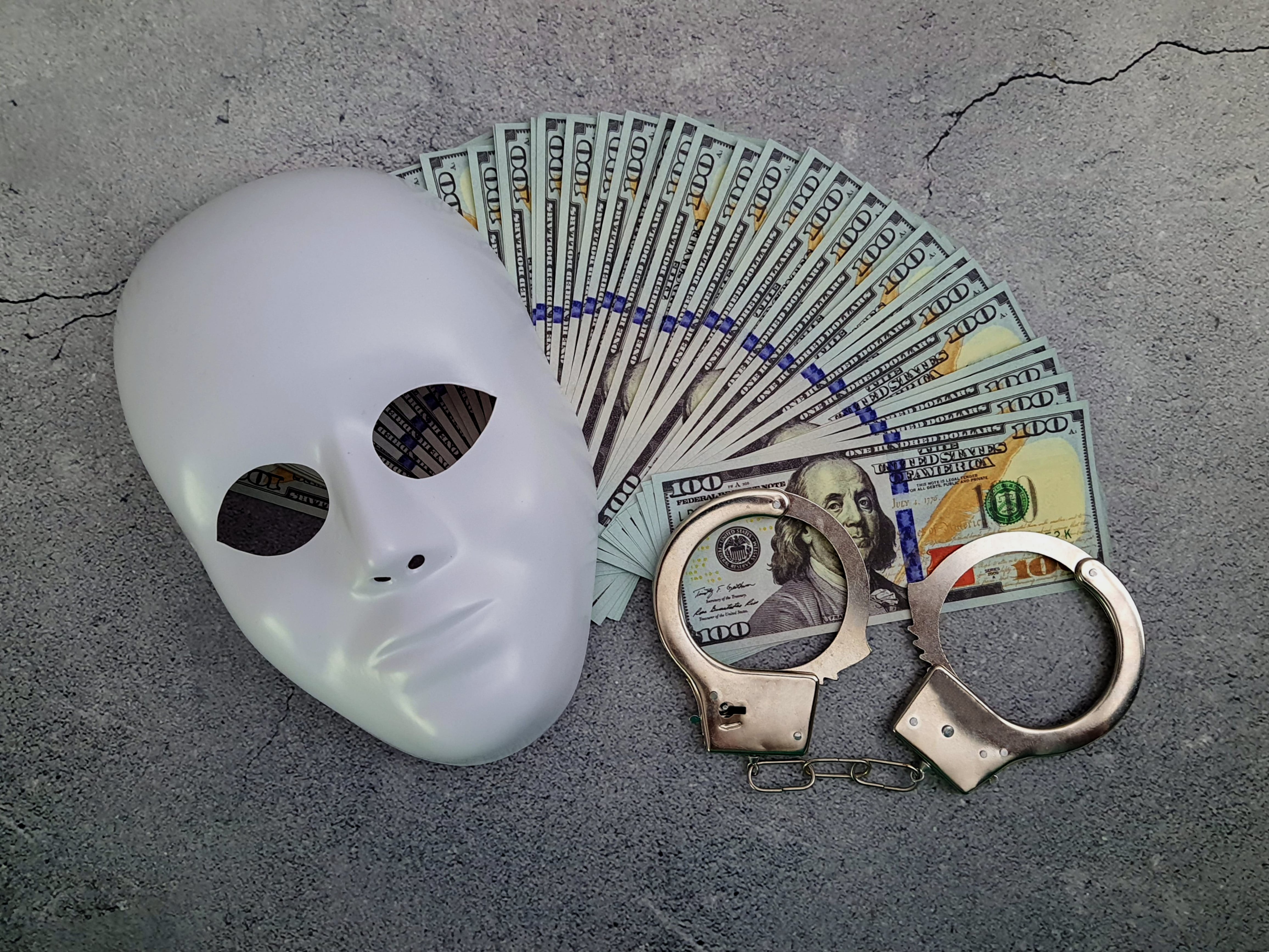 Handcuffs made of hundred-dollar bills with a White plastic mask.