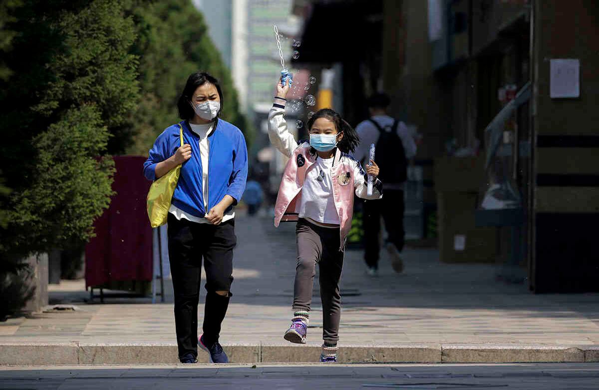 Niño juega con burbujas junto a una mujer, usando tapabocas, mientras caminan por el pavimento en Beijing. Andy Wong / AP