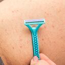 Close up picture of woman holding razor, shaving her hairy leg with folliculitis