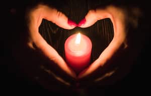 Manos femeninas en forma de corazón alrededor de una vela roja encendida