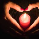Manos femeninas en forma de corazón alrededor de una vela roja encendida
