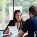 Hispanic businesswoman smiles while showing a document to a male associate.