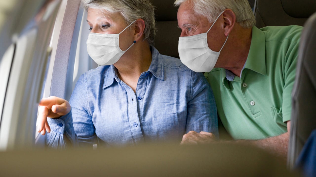 Pareja de ancianos latinoamericanos viajando en avión con mascarillas y mirando por la ventana - viaje durante la pandemia de COVID-19