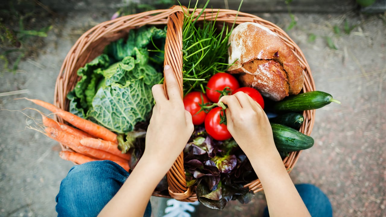 Manos de una niña poniendo vegetales recién cosechados en una canasta