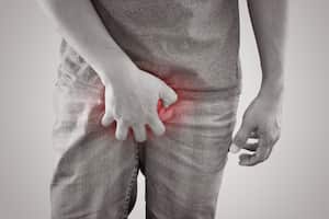 Los hombres asiáticos sostienen la entrepierna contra un fondo gris. Personas con picazón en la entrepierna. Problema del cuerpo humano o concepto de salud y medicina.