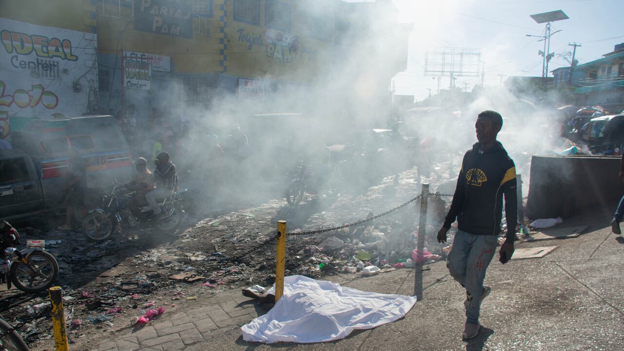 Contenido gráfico / Un hombre pasa junto al cuerpo de una persona que estaba entre una docena asesinada en la calle por pandilleros, en Ptionville, Puerto Príncipe, Haití, el 18 de marzo de 2024.