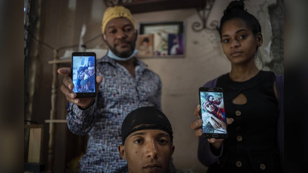 Odlanier Santiago Rodríguez, al centro, quien fue acusado de participar en las protestas de julio del año pasado y fue liberado tras 22 días en prisión, posa para una fotografía junto con su tío Emilio Román, a la izquierda, y la nuera de éste, María Carla Milán Ramos, mientras muestran fotos de los tres hijos de Román que aún permanecen detenidos. La imagen fue tomada en el barrio La Güinera en La Habana, Cuba, el miércoles 19 de enero de 2022 (AP Foto/Ramón Espinosa)