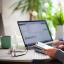 Mujer que trabaja desde casa usando una computadora portátil mientras lee un mensaje de texto en el teléfono móvil