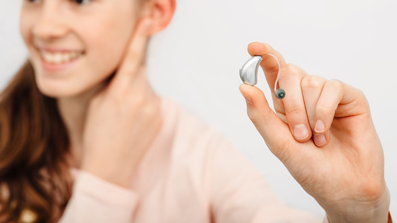 Solución auditiva para niños. Niña sosteniendo un audífono, tratamiento de la sordera en niños. Audiología