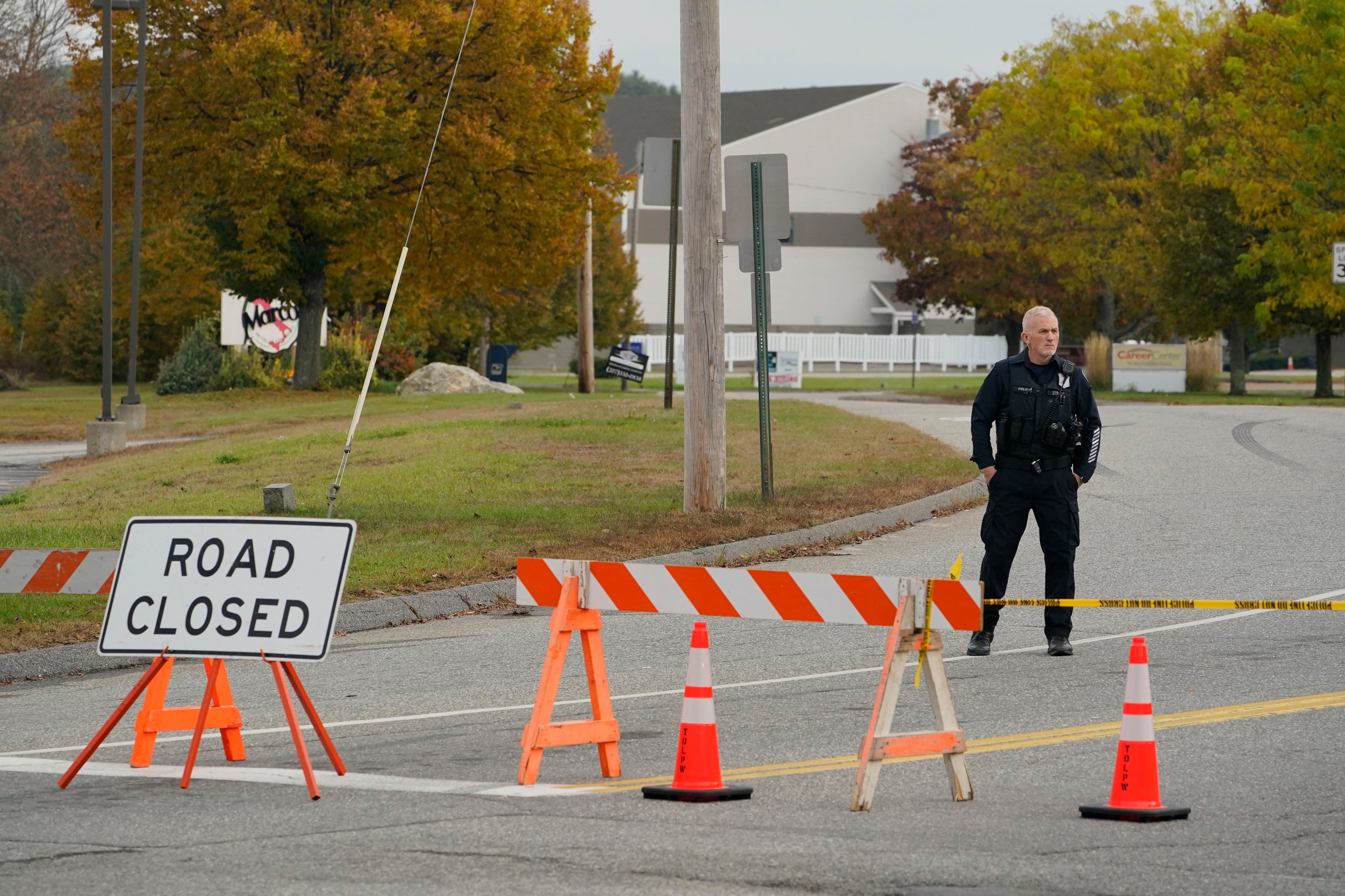 Un oficial de policía se encuentra en un cierre de carretera cerca de una bolera, visto al fondo, el jueves 26 de octubre de 2023, en Lewiston, Maine.