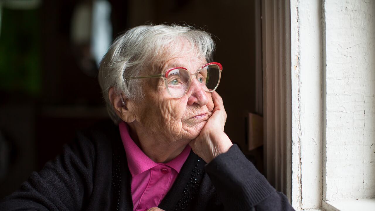 Anciana con gafas mirando pensativamente por la ventana. Abuela pensativa mirando por la ventana.