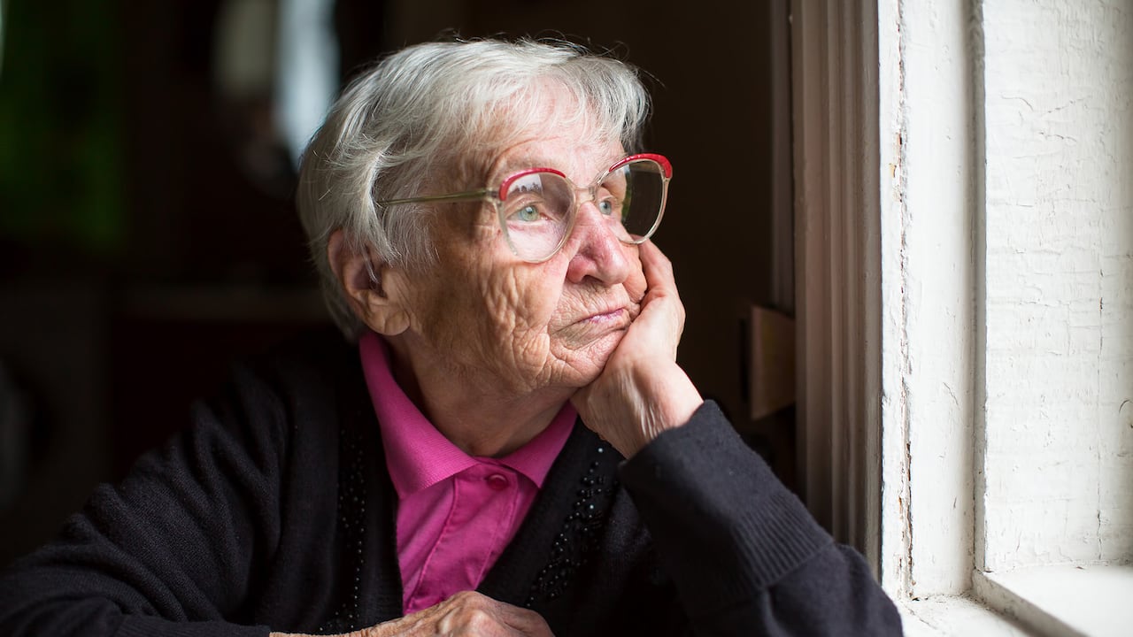 Anciana con gafas mirando pensativamente por la ventana.
