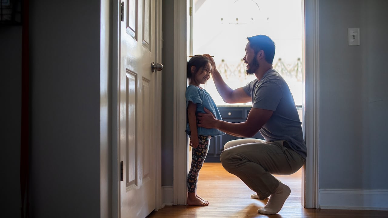 Father measuring daughter's height against wall