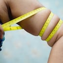 Mujer asiática de mediana edad muestra la grasa corporal del vientre con cinta métrica o cinta de línea con pantalón deportivo.