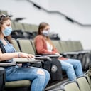 Grupo multiétnico de estudiantes que usan máscaras protectoras mientras están sentados en una sala de conferencias a 2 metros de distancia.