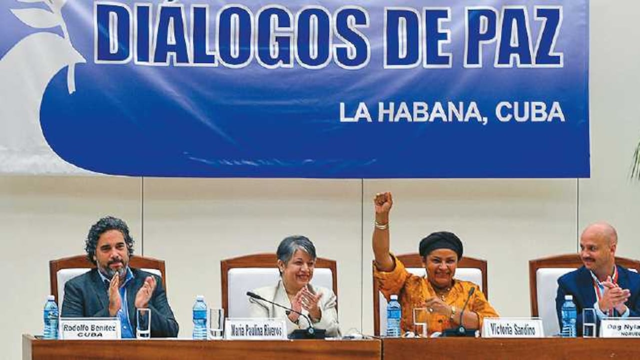 Victoria Sandino, de las Farc, hace una señal de triunfo por el acuerdo. A su lado, María Paulina Riveros y los garantes.