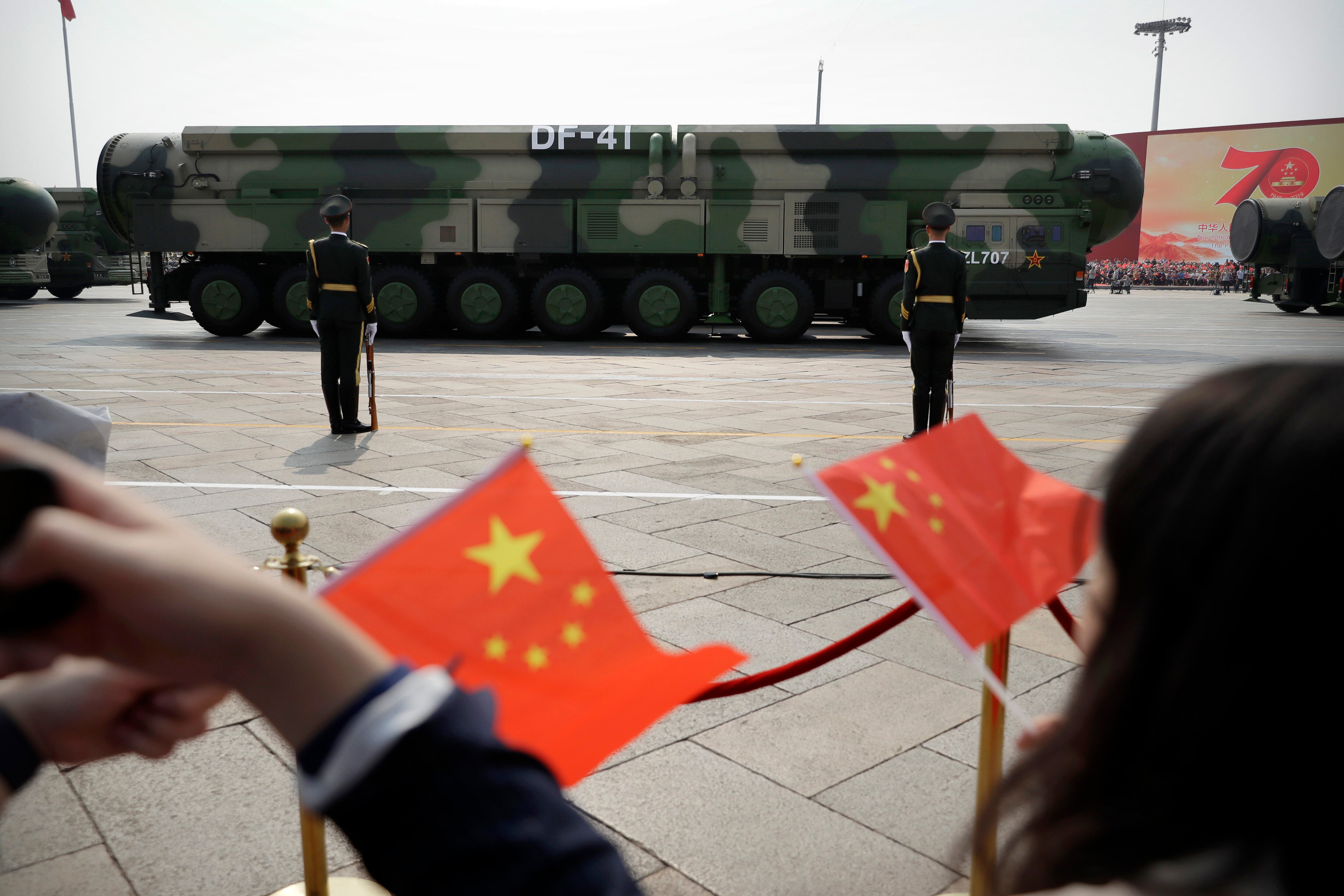 Espectadores ondean banderitas chinas mientras vehículos militares con misiles balísticos DF-41 pasan durante un desfile en ocasión del 70mo aniversario de la fundación del Partuido Comunista de China en Beijing. (AP Foto/Mark Schiefelbein)