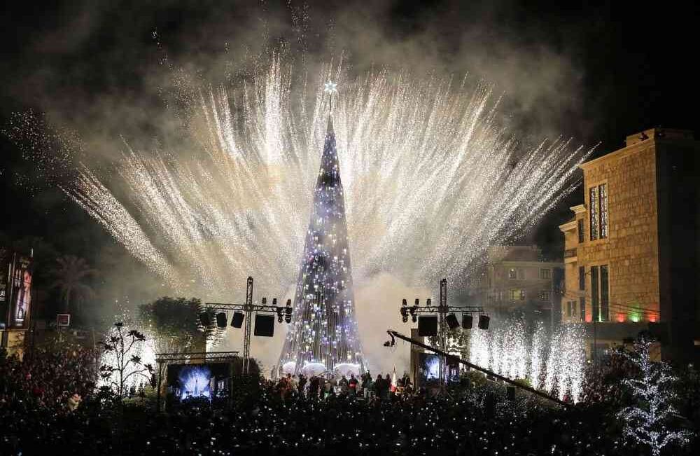 Las personas se reúnen y usan sus teléfonos celulares para filmar fuegos artificiales mientras iluminan el cielo durante la iluminación de un árbol de Navidad en una plaza en la ciudad costera libanesa de Byblos, al norte de Beirut, el 30 de noviembre de 2017. / AFP PHOTO / JOSEPH EID