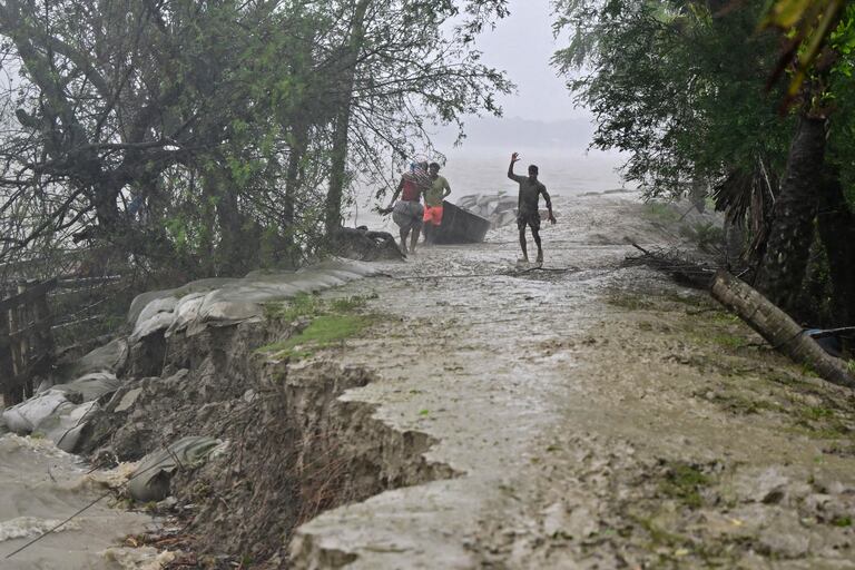 La gente camina sobre un terraplén dañado a lo largo del río Sonatola durante las fuertes lluvias en Patuakhali el 27 de mayo de 2024, tras la llegada a tierra del ciclón Remal en Bangladesh.