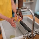 Close-up of a man and woman hands washing a glass under running water in sink at home. Romantic couple watching dishes in kitchen at home.