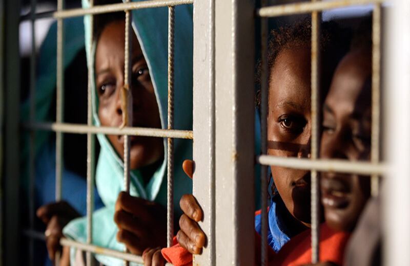 Migrantes rescatados frente a las costas de Libia en un barco noruego se asoman para conseguir la primera vista de la isla de Cerdeña, ya que navegan en el mar Mediterráneo hacia el puerto italiano de Cagliari.