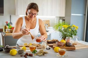 Mature woman pouring honey in ginger and lemon hot tea cup