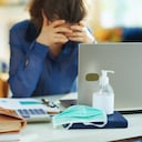 Primer plano de una máscara médica y desinfectante de manos y una mujer estresada en segundo plano en la oficina en casa temporal durante la epidemia de coronavirus en la casa en un día soleado.