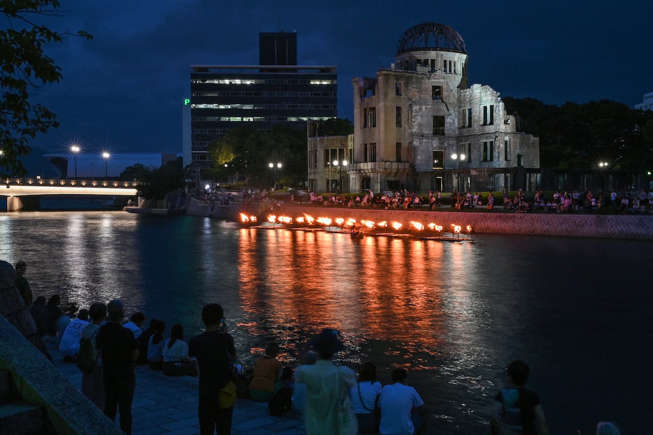 La gente observa cómo se encienden pequeñas hogueras a lo largo del río Motoyasu frente a la Cúpula de la Bomba Atómica durante una ceremonia en memoria de las víctimas en vísperas del 80º aniversario del primer ataque con bomba atómica del mundo, en la ciudad de Hiroshima el 5 de agosto de 2025. (Foto de Richard A. Brooks / AFP)