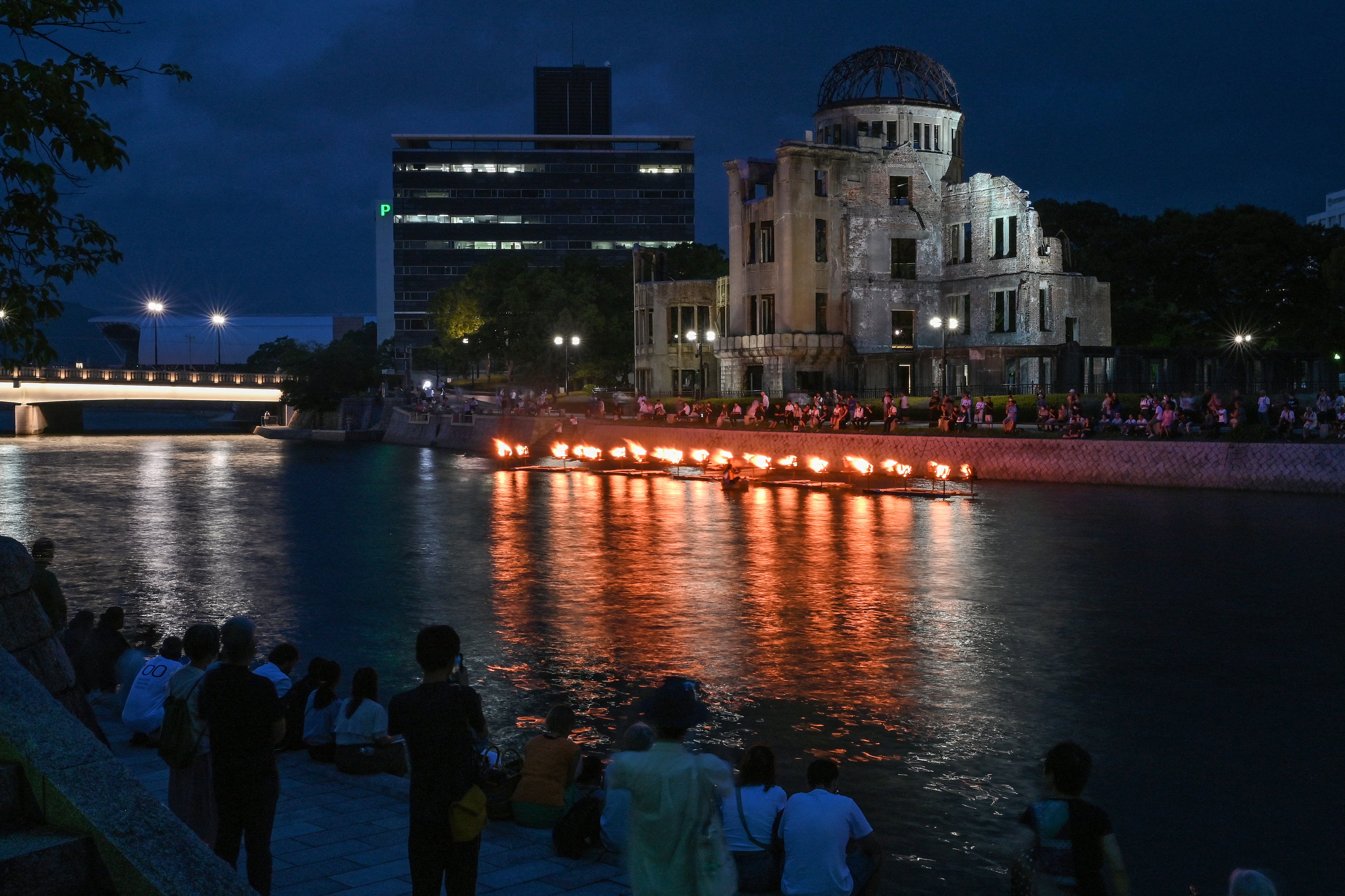 La gente observa cómo se encienden pequeñas hogueras a lo largo del río Motoyasu frente a la Cúpula de la Bomba Atómica durante una ceremonia en memoria de las víctimas en vísperas del 80º aniversario del primer ataque con bomba atómica del mundo, en la ciudad de Hiroshima el 5 de agosto de 2025. (Foto de Richard A. Brooks / AFP)