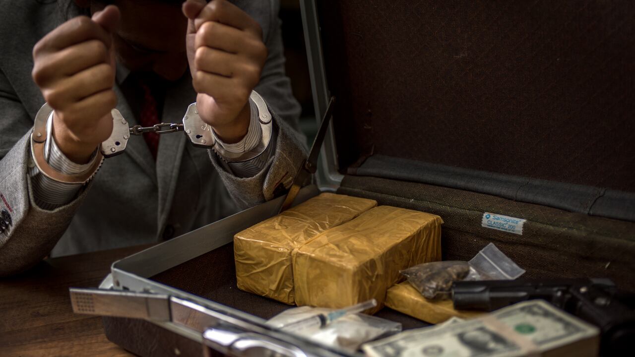El narcotraficante fue arrestado y esposado, con paquete de drogas, billete y pistola sobre mesa de madera.