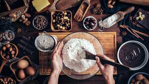 Manos de mujer haciendo mousse de chocolate y galletas en una mesa de madera en una cocina rústica