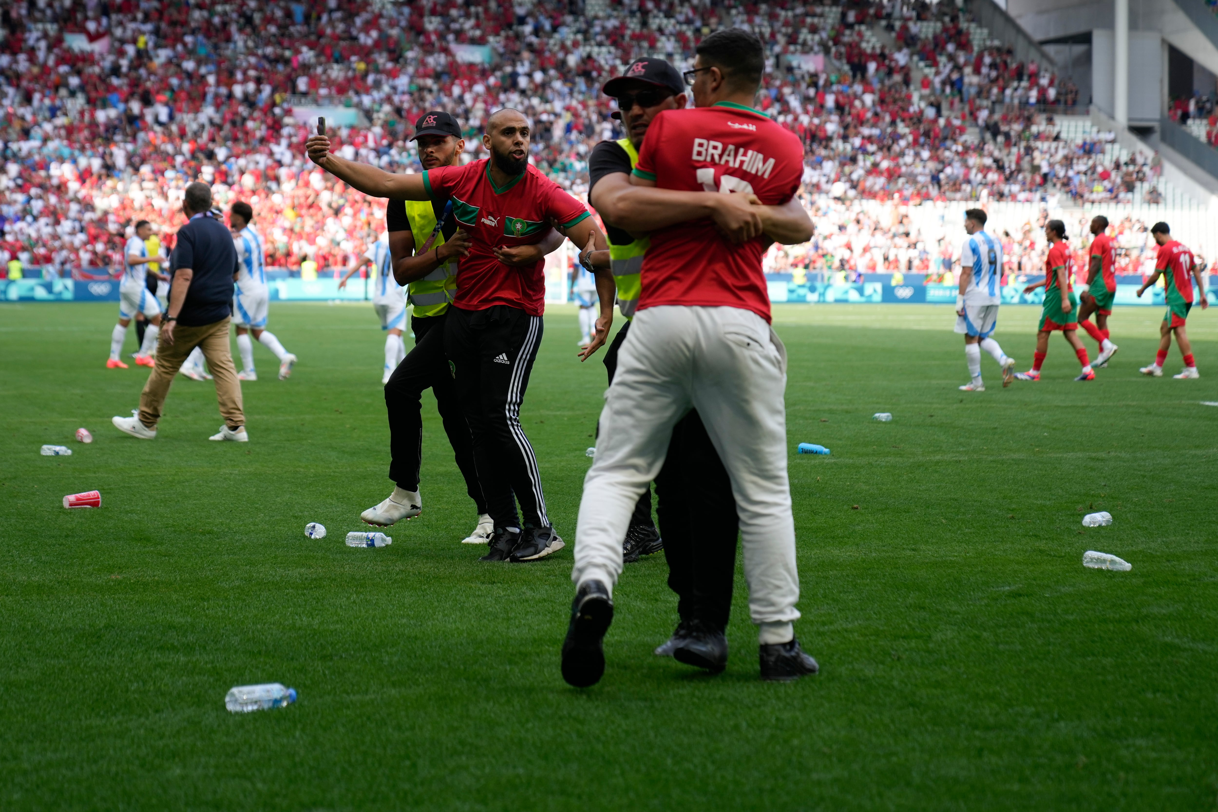 Stewards catch pitch invaders during the men's Group B soccer match between Argentina and Morocco at Geoffroy-Guichard Stadium at the 2024 Summer Olympics, Wednesday, July 24, 2024, in Saint-Etienne, France. (AP Photo/Silvia Izquierdo)