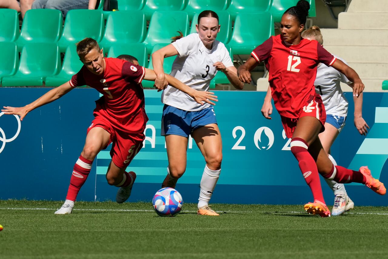 La neozelandesa Mackenzie Barry (centro) compite por el balón con las canadienses Quinn (izquierda) y Jade Rose durante el partido de fútbol femenino del Grupo A entre Canadá y Nueva Zelanda en el estadio Geoffroy-Guichard durante los Juegos Olímpicos de Verano de 2024, el jueves 25 de julio de 2024, en Saint-Etienne, Francia. (Foto AP/Silvia Izquierdo)